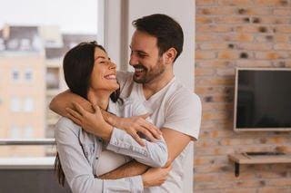 A man and woman hugging in front of a brick wall.