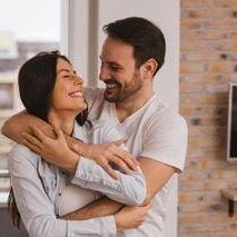 A man and woman hugging in front of a brick wall.